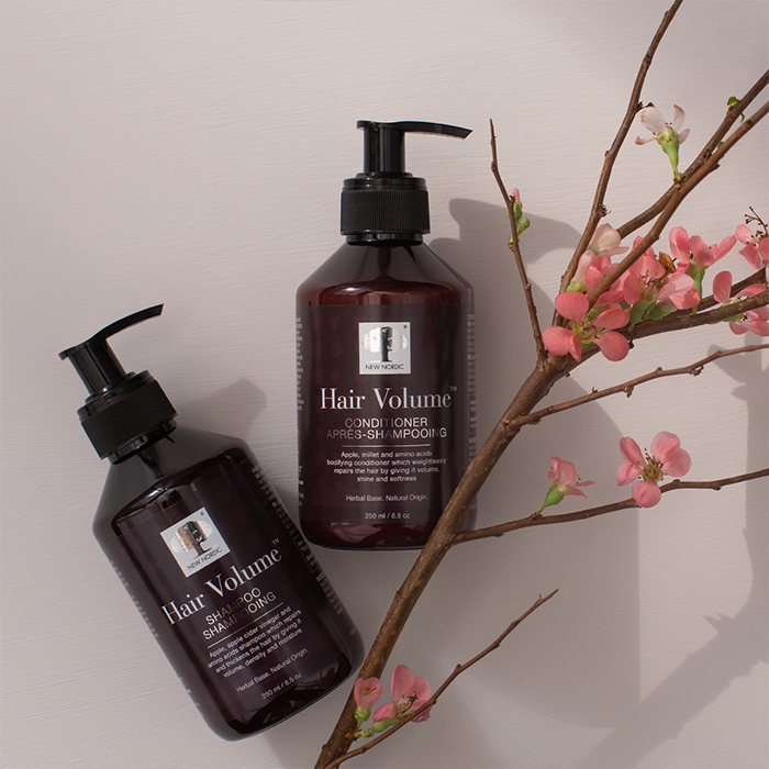New Nordicin Hair Volume shampoo ja hoitoaine pullot kumollaan pöydällä, vieressä kukkiva omenapuunoksa. FI - Hair Volume™ Shampoo & Conditioner