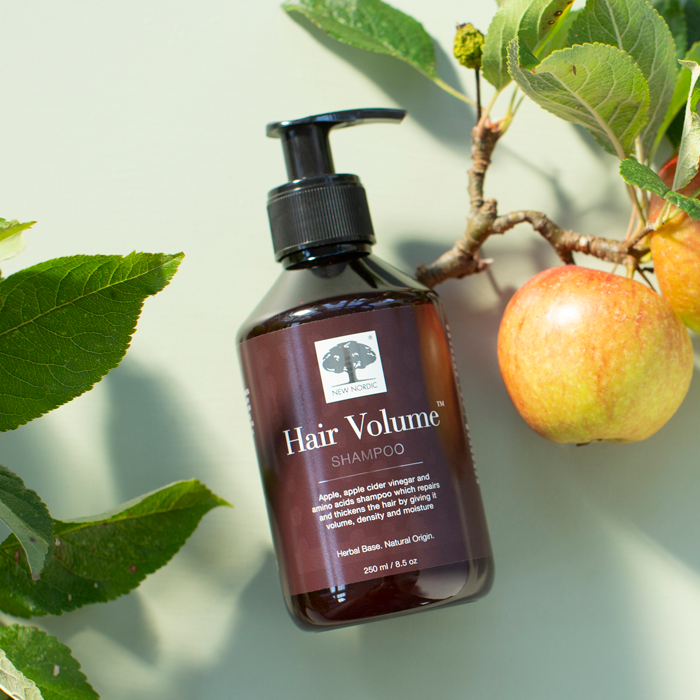 New Nordicin kosteuttavan shampoon pullo aseteltuna kumolleen pöydälle omenapuunoksien ja omenoiden ympäröimänä. FI OLD - Hair Volume™ Shampoo