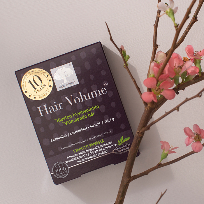 Hair Volume™ hiusravinne pakkaus: hiusten hyvinvointiin tarvittavia vitamiineja. Paketin vieressä kukkivan omenanpuun oksa. FI - Hair Volume™ - 90 tabl.